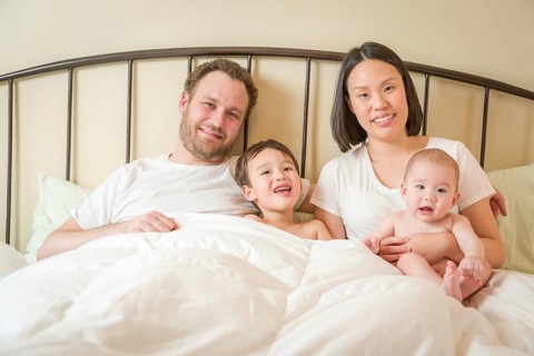 Young mixed-race chinese and caucasian baby boys laying in bed with their father and mother