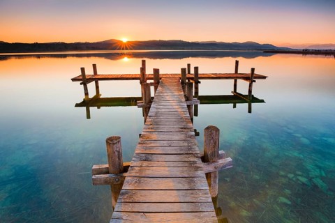 Holzsteg am Pfaeffikersee im Gegenlicht bei Sonnenaufgang mit Blick zum Bachtel und Glaernisch im Hintergrund