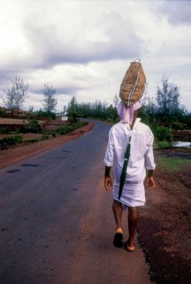 A man carrying bag over his head and an umbrella behind his shirt on the road
