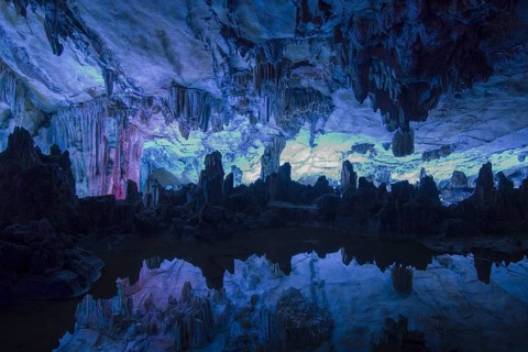 Interior of a limestone cave with stalactites and stalagmites reflected in a pond