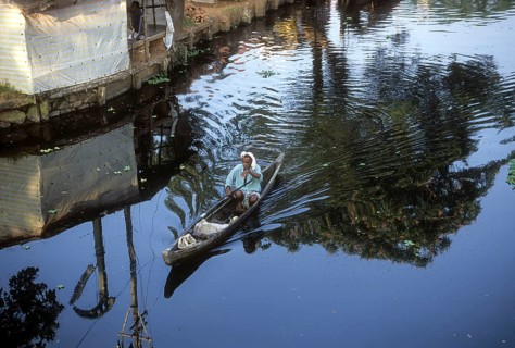 A fisherman rowing a sailboat using a stick in backwaters of kerala