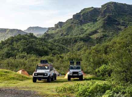 Two white Land Rover off-road vehicles on a campsite with tents