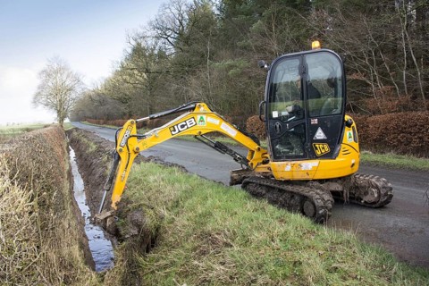 Cleaning overgrown roadside drainage ditches with a JCB excavator