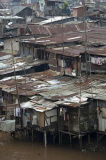 Stilted shacks with corrugated iron roofs beside river in city