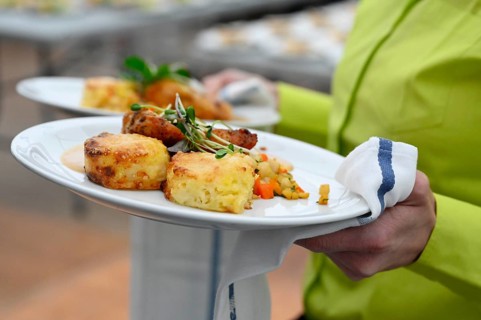 Service staff with plate of corn poulard breast with potato gratin and root vegetables