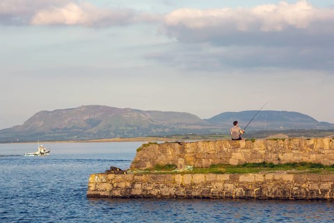 Man rod fishing on summers evening as boat heads out to sea. Sligo