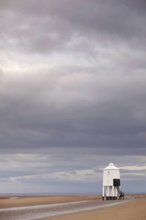 Rain clouds and low wooden pole lighthouse on the beach at low tide