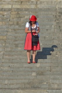 Woman in red dirndl stands on stairs and looks into mobile phone