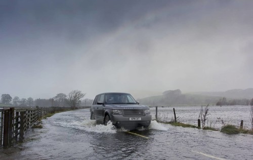 Range Rover driving on road flooded during heavy rain