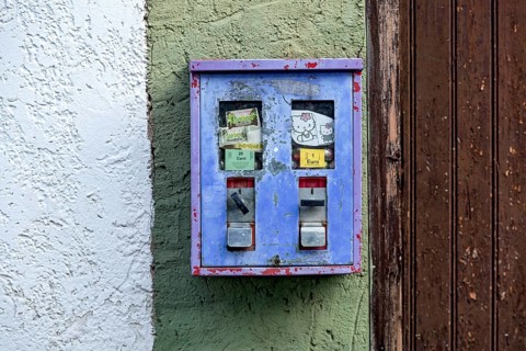 Old chewing gum machine filled with chewing gum and children's toys on the wall of a house
