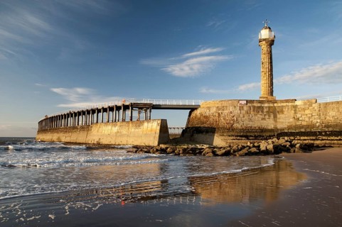 View of beach and pier with 19th century stone lighthouse in the evening sun