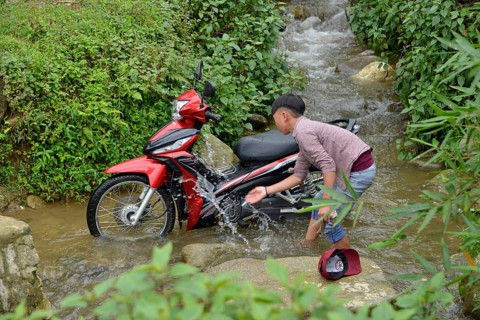 Boy washes motorbike in stream
