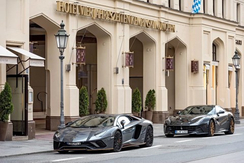 Parked Lamborghini Aventador and Ferrari F12 Berlinetta sports cars in front of Hotel Vier Jahreszeiten Kempinski