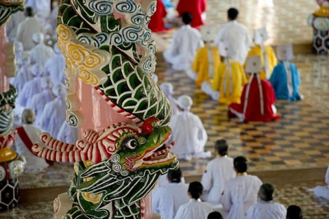 Caodaist disciples sitting beside colourful columns with dragons during ceremony