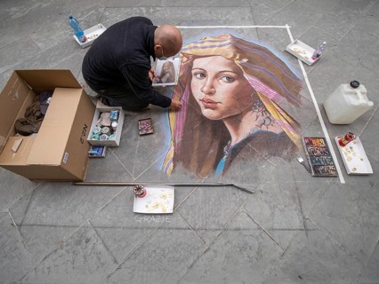 Strassenkuenstler malt ein Bild mit Kreide auf den Asphalt