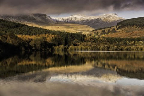 Trees and snow-capped hills reflected in the reservoir at sunrise