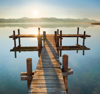 Holzsteg am Pfaeffikersee im Gegenlicht bei Sonnenaufgang mit Blick zum Bachtel und Glaernisch im Hintergrund