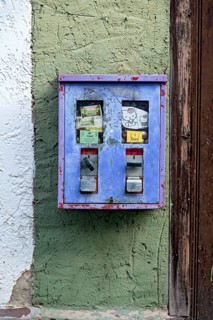 Old chewing gum machine filled with chewing gum and children's toys on the wall of a house