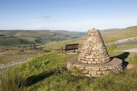 Cairn and bench at highland viewpoint overlooking valley marking Muker parish boundary