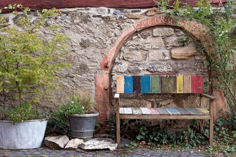 Old colourfully painted faded wooden bench and planter on house wall