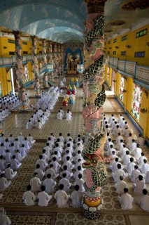 Caodaist disciples sitting beside colourful columns with dragons during ceremony