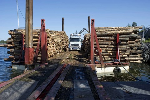 Lorry with grapple loading logs onto timber barge