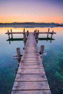 Holzsteg am Pfaeffikersee im Gegenlicht bei Sonnenaufgang mit Blick zum Bachtel und Glaernisch im Hintergrund