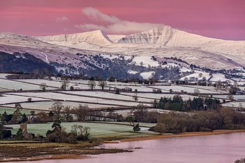View of snow covered farmland and hills at sunrise