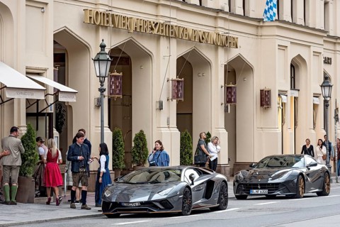 Parked Lamborghini Aventador and Ferrari F12 Berlinetta sports cars in front of Hotel Vier Jahreszeiten Kempinski