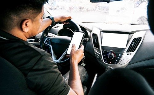 Person holding the cell phone and with the other hand the steering wheel