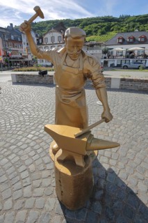 Golden sculpture as goldsmith and locksmith working steel at an anvil with hammer in Alf
