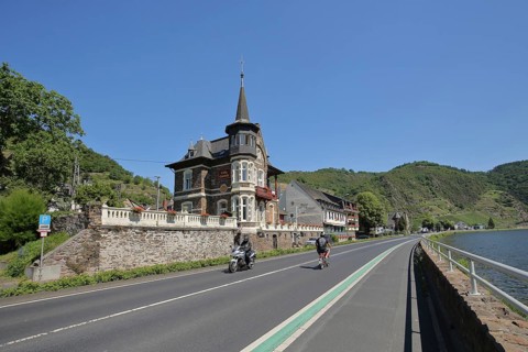 Villa Cornely with motorcyclist and cyclist on the road in Treis-Karden on the Lower Moselle