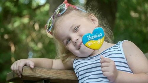 Little blonde girl holds gingerbread in Ukrainian national colors in her hand
