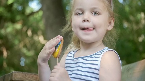 Little blonde girl holds gingerbread in Ukrainian national colors in her hand