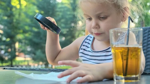 Little girl carefully looks into the lens at the salt. Close-up of blonde girl is studying salt crystals while looking at her through magnifying glass while sitting in street cafe in the park. Â Odess...