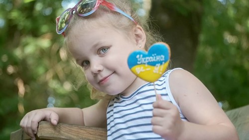 Little blonde girl holds gingerbread in Ukrainian national colors in her hand
