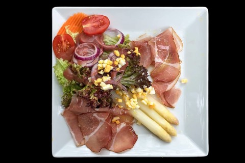 Asparagus salad with ham on a black background