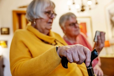 Senior citizen with crutch is shown a smartphone by her sister