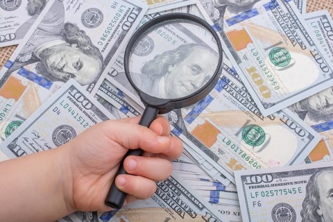 Magnifying glass is held over the banknote bundle of US dollar