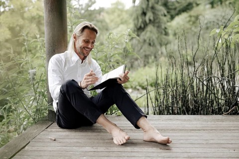 Businessman in white shirt sits on wooden jetty and writes in a book,