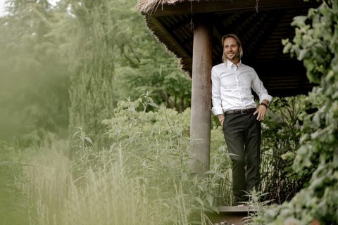 Businessman in a white shirt stands on the wooden jetty in the greenery,