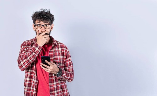 Man holding his cell phone and covering his mouth. surprised man receiving news on his cell phone isolated. Astonished man holding his cellphone and covering his mouth isolated,