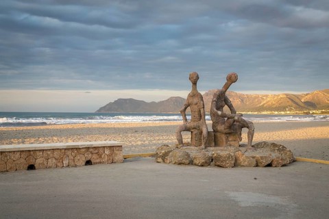 Sculptures by Joan Bennassar on beach promenade with sandy beach Playa Sa Canova in Son Serra de Marina, Serres de Llevant mountains in the back