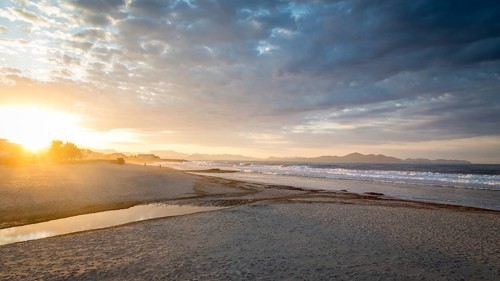Sunset at the sandy beach playa in Son Serra de Marina, Tramuntana Mountains in the back