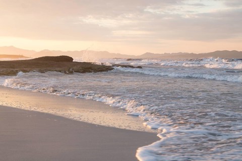 Sunset and breaking waves at the sandy beach playa in Son Serra de Marina, Tramuntana Mountains in the back