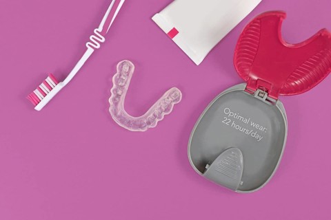 Customized transparent teeth bite guard clear aligners for lower jaw with storing case, tooth brush and paste on pink background