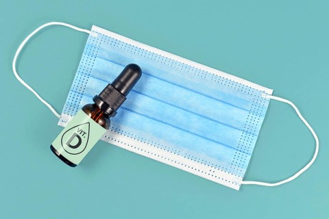 Vitamin D helping fight Corona virus illness. Concept with medical face mask and bottle with vitamin drops on blue background,