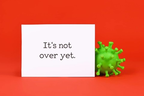 Corona virus model and note with text 'It's not over yet' on red background,