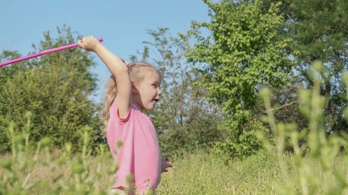 Little girl plays with butterfly net of tall grass in city park. Cute little girl is playing with aerial insect net in meadow on sun day. Odessa, Ukraine