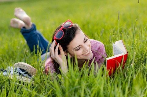 Young woman lying in meadow and reading a book,